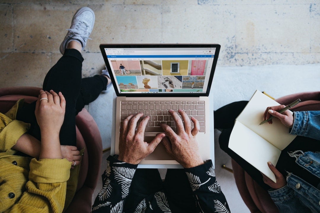 Aerial image of three people sitting around a laptop with stock images on the screen