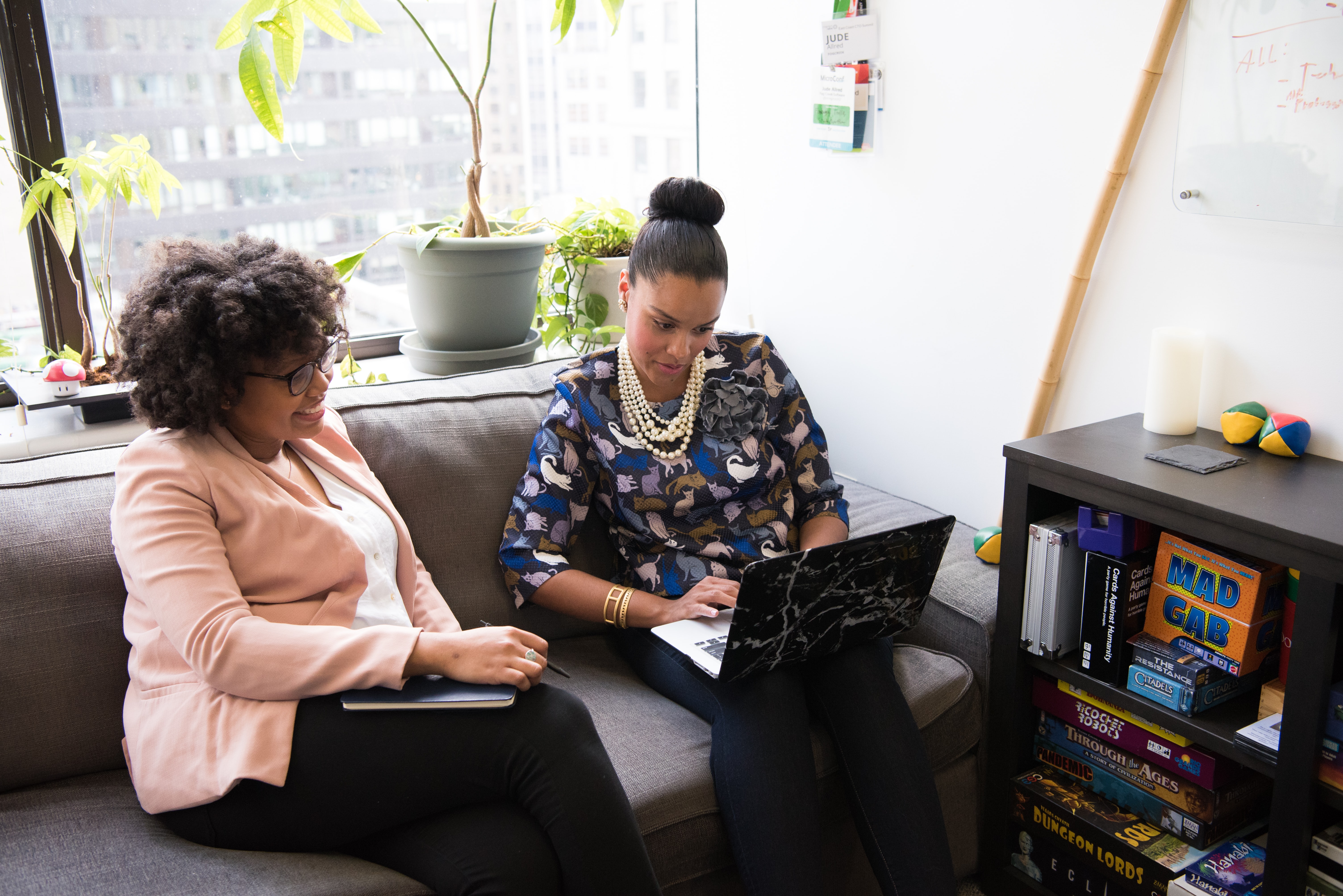 Two women looking at a laptop on a couch in a casual workspace